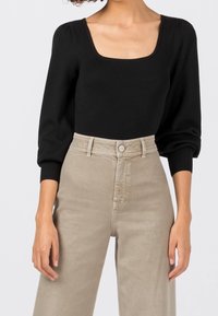 Haut noir côtelé à manches longues avec un col carré, associé à un pantalon large taille haute beige clair avec fermeture à boutons.