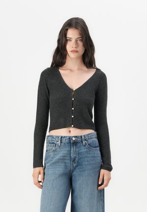Grijze, cropped cardigan met lange mouwen, V-hals en parelknoopjes aan de voorkant; gecombineerd met hoge taille blauwe jeans.