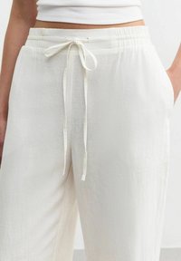 Pantalones ligeros de color crema con una cinturilla elástica y cordón ajustable, que cuentan con bolsillos laterales y una tela suave y texturizada.