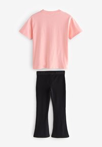 Lyserød bomulds-t-shirt med rund halsudskæring og korte ærmer, kombineret med sorte elastiske leggings med en logo-strækbånd i taljen og udvidede manchetter.