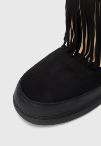 Melna zamšāda zābaks ar noapaļotu purngalu, šūtu ādas zoli un dekoratīvām frizēm augšējā priekšpusē.