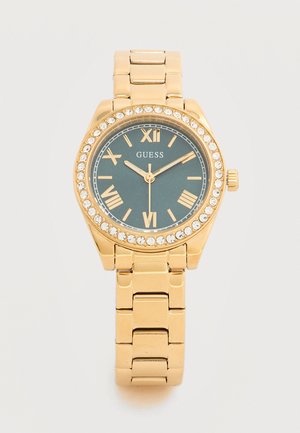 Montre-bracelet Guess ton or avec cadran foncé, chiffres romains, lunette en cristal et bracelet en métal à maillons, affichant 10:10:36.