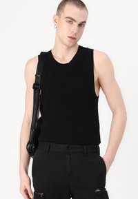 Svart ermeløs topp i ribbet stoff, tettsittende design. Kombinert med svarte bukser med sidelommer med glidelås og en svart skulderveske.