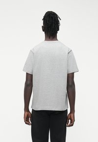 Pilka trumpomis rankovėmis medvilninė palaidinė. Turi apvalų kaklo iškirpimą ir laisvo stiliaus siluetą, matomos siūlės ant pečių siūlių.