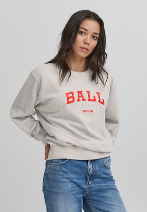 Szürke pulóver piros "BALL 1974 THE JEANS" felirattal az elején, kerek nyakkivágással és bordás mandzsettákkal. Kék farmernadrággal viselve.