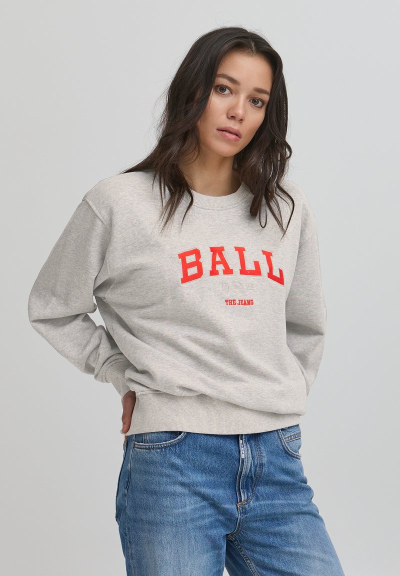 Pilkas džemperis su raudonu tekstu "BALL 1974 THE JEANS" ant priekio, su apvalia iškirpte ir gumele prie rankovių. Dėvimas su mėlynais džinsais.