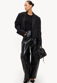 Blazer negro oversize, top negro ajustado, pantalones anchos de faux cuero negro brillante de talle alto, bolso negro pequeño con tachuelas, zapatos negros de punta.