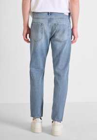 Jeans de mezclilla azul claro con un corte relajado, piernas rectas y bolsillos traseros visibles. Presentados con una camiseta blanca sencilla y zapatos claros.