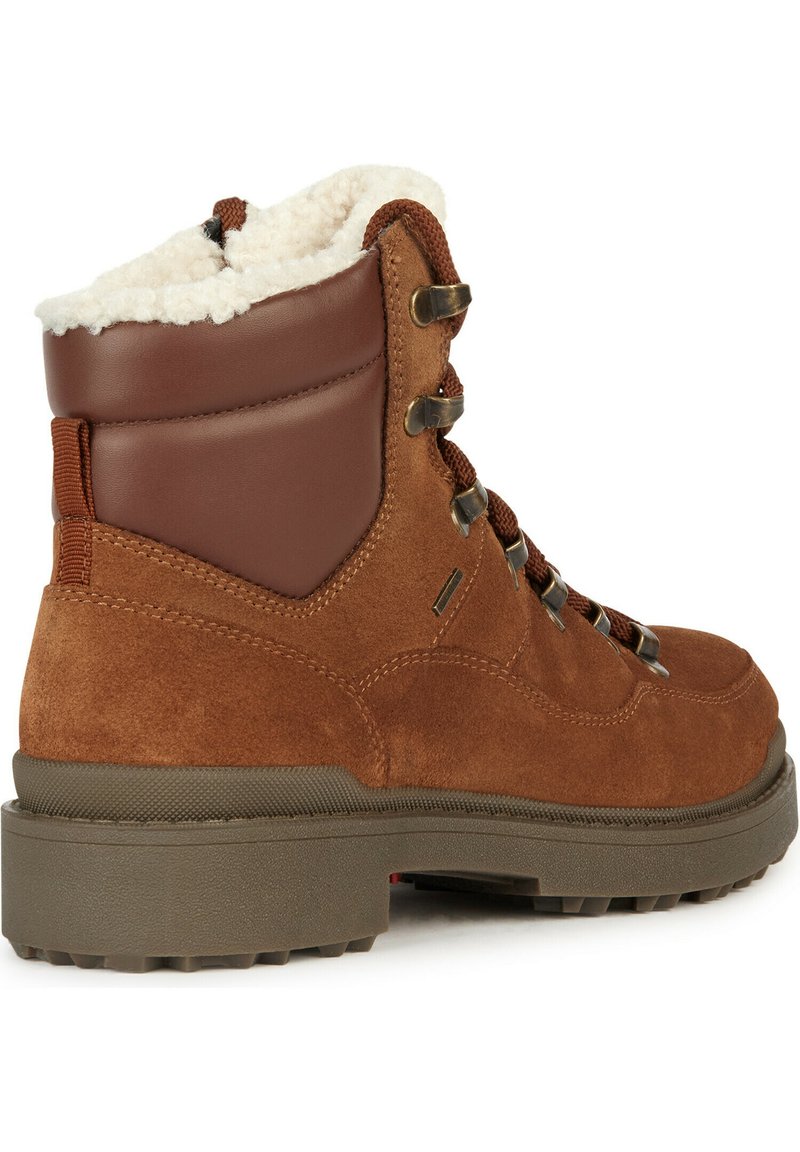 Botte de randonnée en suede marron avec un col rembourré en cuir marron, doublure en fausse fourrure, œillets en métal et une épaisse semelle en caoutchouc grise.