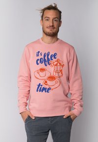 Sweatshirt rose avec un texte imprimé bleu et orange et des illustrations de tasses à café. Poignets et ourlet côtelés, col rond. Coupe décontractée.