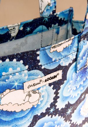Blauwe stoffen draagtas met speelse Moomin-figuren en een patroon van een sterrenhemel, voorzien van een Cath Kidston x Moomin-label.