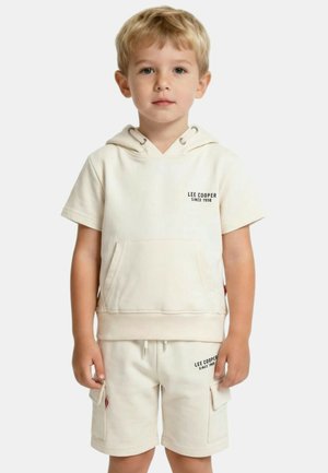 Jeune garçon portant un sweat à capuche à manches courtes de couleur crème et un short cargo assorti avec les logos "Lee Cooper Since 1908".