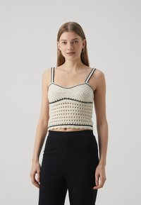 Top corto all'uncinetto color crema con rifiniture nere, caratterizzato da un design testurizzato con trame aperte e spalline a spaghetti regolabili. Pantaloni neri a coste.