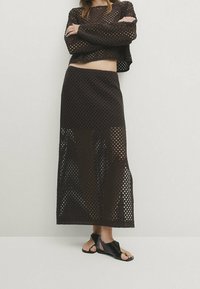 Braunes zweiteiliges Strickset mit einem cropped Langarmoberteil mit quadratischem Ausschnitt und einem langen Rock mit ähnlichem offenem Strickmuster.