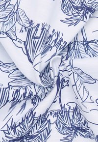 Witte stof met marineblauwe botanische lijntekeningen, waaronder bladeren en takken, verzameld en gedraaid in het midden.
