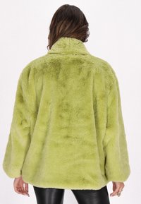 Giacca in pelliccia sintetica verde lime con colletto alto, vestibilità ampia e superficie morbida e testurizzata. Maniche lunghe e orlo arrotondato.