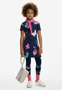 Abito navy con stampe di frutta colorata e farfalle, abbinato a leggings scuri e una sciarpa rosa. Gli accessori includono una borsa grigia chiara.