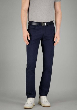 Marineblau strukturierte Hose im Slim-Fit-Stil, kombiniert mit einem grauen T-Shirt und einem schwarzen Gürtel. Weiße Sneaker vervollständigen das Outfit.