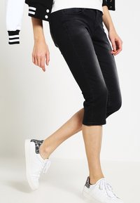 Pantalones capri de mezclilla negra con un ajuste slim, con una cintura de media altura y un ligero desvanecimiento. Combinados con zapatillas blancas con un talón estampado.