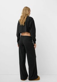 Sort ribbet cropped sweater parret med matchende brede bukser. Materialet ser blødt ud med en tekstureret finish. Skoene er lysebrune.
