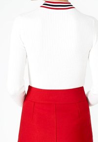Haut blanc côtelé à manches longues avec un col rayé et une jupe rouge taille haute avec des coutures latérales et une texture lisse.