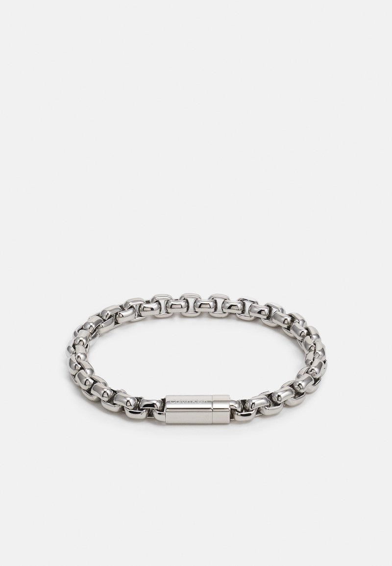 Hõbedane metallkäevõru, mis sisaldab omavahel seotud linke läikiva viimistlusega ja silindrilist lukku. Sile tekstuur kergelt peegeldava pinnaga.