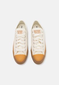 Canvas sneakers with a cream upper and orange rubber toe cap. Features white laces, silver eyelets, and a brown rubber sole.