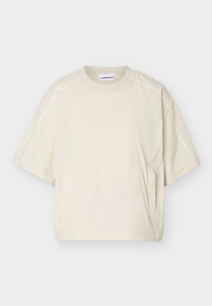 Chemise beige à manches courtes avec col rond, détails de coutures blanches sur les épaules et les manches, et poche latérale sur un fond uni.