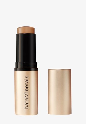 Stick fond de teint BareMinerals avec un boîtier noir et or métallique et un capuchon assorti à côté, sur un fond blanc.