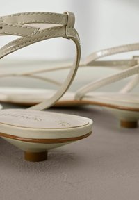 Sandales plates beiges à lanières avec des talons ronds et bas reposant sur une surface grise texturée.