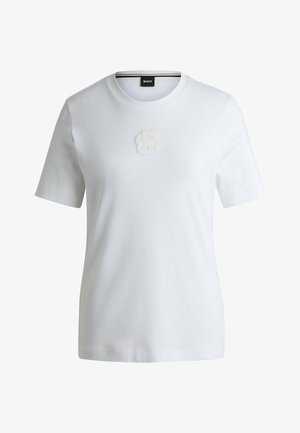 T-shirt bianco in cotone con maniche corte, caratterizzato da un sottile logo ricamato al centro. Collo a giroclassico con una texture liscia.