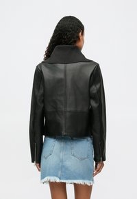 Μαύρο δερμάτινο μπουφάν με ψηλό γιακά, στενή γραμμή και μακριά μανίκια, συνδυασμένο με φθαρμένη τζιν φούστα.