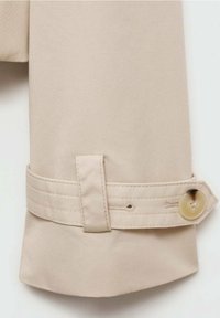 Manche d'un trench-coat beige présentant un poignet avec un bouton, des surpiqûres horizontales et une texture de tissu lisse.