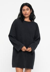 Czarna, oversize sukienka T-shirt wykonana z bawełny. Posiada długie rękawy, okrągły dekolt oraz luźny krój, z gładką teksturą.