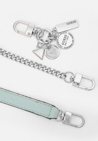 Cadena de plata y correa de cuero azul claro con cierres metálicos, que presenta encantos circulares y rectangulares de la marca GUESS.