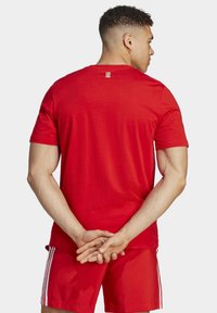 Camiseta roja de manga corta, hecha de algodón. Presenta un pequeño logo en la parte superior de la espalda y un clásico escote redondo.