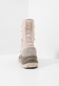 Béžová hikingová bota s texturovanou suede patou, polstrovaným límcem a zpevněnými rýčkami. Má pevných gumovou podrážku pro trakci.