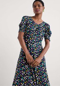 Robe florale avec un fond sombre et des motifs de tulipes multicolores. Manches courtes bouffantes, encolure large et coupe au genou.