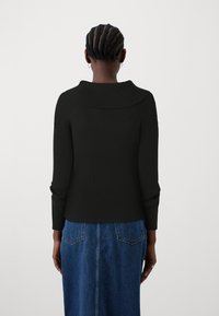 Pull noir à côtes avec un large col, une silhouette ajustée, et des manches longues, associé à une jupe en denim bleue midi.