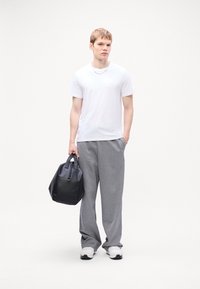 White t-shirt, gray wide-leg sweatpants, and black leather bag. Model wearing white sneakers with black soles. Minimalist design, casual look.