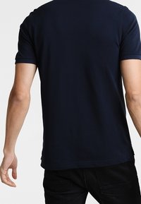 Camiseta de manga corta azul marino con escote redondo, mostrada desde la parte posterior, que presenta una textura suave y un sutil detalle en el dobladillo.