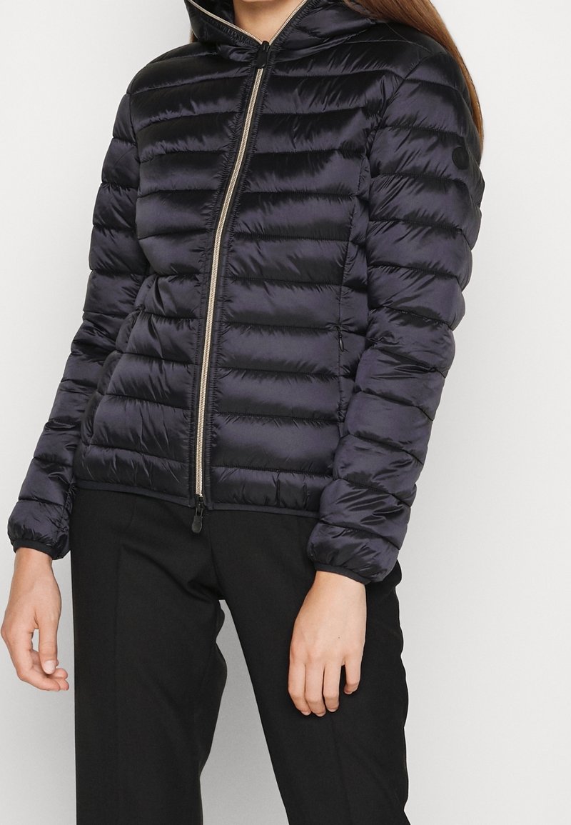 Marineblaue Steppjacke mit Reißverschluss, Kapuze und gestepptem Design. Verfügt über elastische Bündchen und Seitentaschen für zusätzlichen Nutzen.