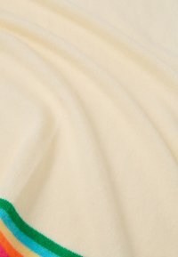 Kremowa tkanina o miękkiej fakturze, z kolorowym paskiem u dołu w zielonym, niebieskim, różowym i pomarańczowym kolorze.