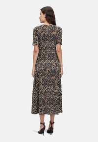 Midi šaty s leopardím potiskem a krátkým rukávem, vyrobené z elastického materiálu, s kulatým výstřihem a siluetou do A. Na nohou černé vysoké podpatky.