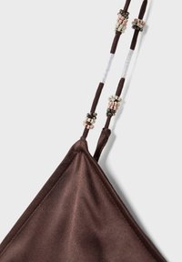 Triangle en tissu marron avec des fines bretelles ornées de petites perles roses, blanches et noires sur un fond blanc.