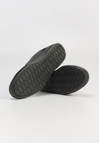 Czarne buty na gumowej podeszwie z teksturowanym bieżnikiem, z eleganckim wzornictwem górnej części i minimalistycznym profilem.