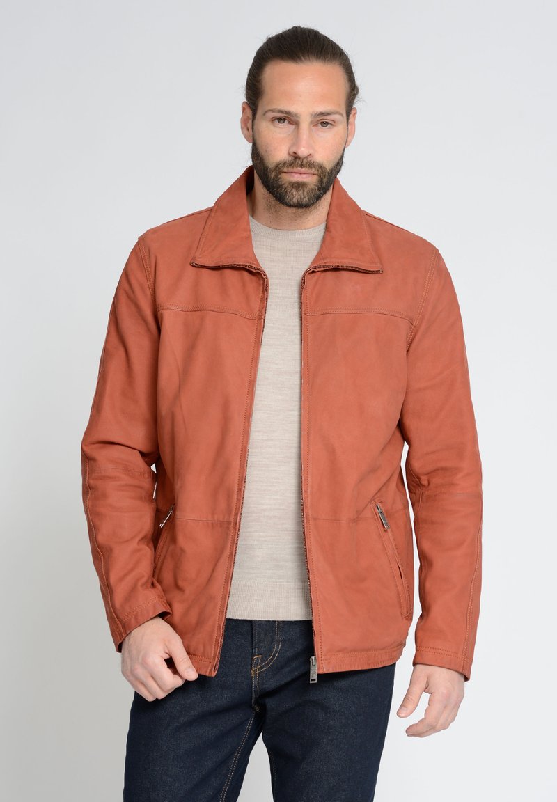 Rostfarbene Lederjacke mit glatter Textur, seitlichen Reißverschlusstaschen und Stehkragen, getragen über einem hellgrauen Hemd.