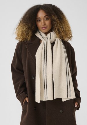 Knit scarf in cream with black stripes, textured fabric, draping around the neck. Worn with a brown double-breasted coat.