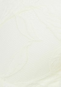 Weißer Stoff mit einer strukturierten Webart, der schlichte, florale Stickmuster zeigt, die der Oberfläche Tiefe und visuelles Interesse verleihen.