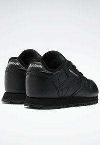 Svarta Reebok-sneakers med lädermaterial, lågt snitt, texturerade accenter och en gummisula med greppgropar.